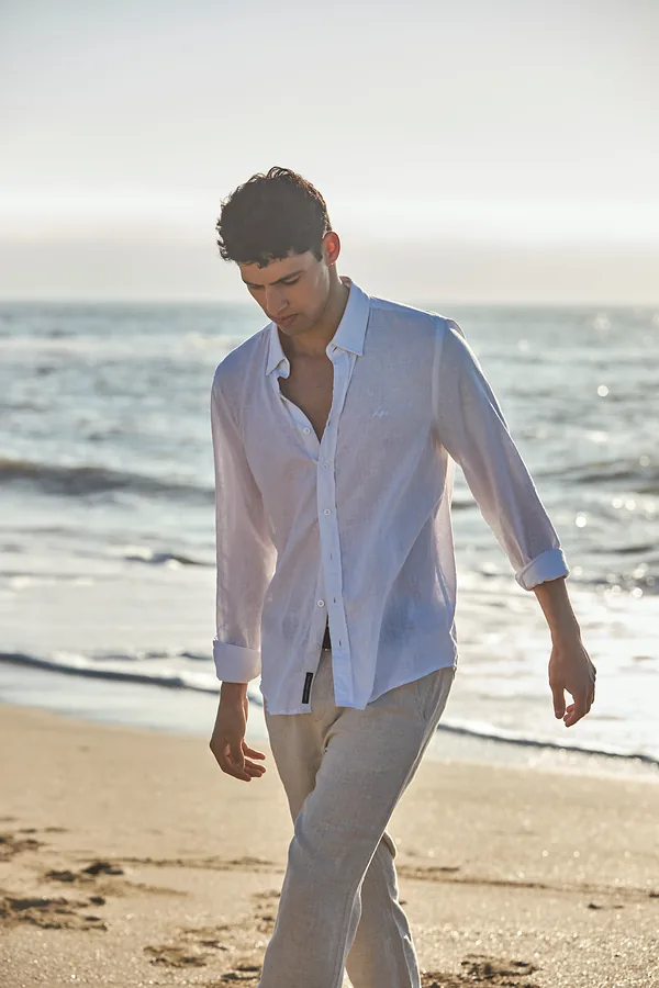 Hombre con camisa de lino blanca caminando por la playa